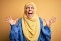 Young beautiful brunette muslim woman wearing arab hijab over isolated yellow background crazy and mad shouting and yelling with Royalty Free Stock Photo