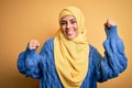Young beautiful brunette muslim woman wearing arab hijab over isolated yellow background Dancing happy and cheerful, smiling Royalty Free Stock Photo