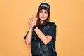 Young beautiful brunette policewoman wearing police uniform bulletproof and cap Holding symbolic gun with hand gesture, playing Royalty Free Stock Photo