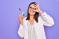 Young beautiful brunette scientist woman wearing coat and glasses holding test tube smiling happy doing ok sign with hand on eye Royalty Free Stock Photo