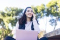 Portrait of a young beautiful brunette sitting on park with laptop while using smartphone to call Royalty Free Stock Photo