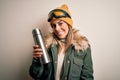 Young beautiful brunette skier woman wearing ski goggles drinking thermo with coffe with a happy face standing and smiling with a Royalty Free Stock Photo