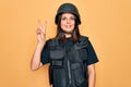 Young beautiful brunette soldier woman wearing bulletproof and security helmet smiling with happy face winking at the camera doing Royalty Free Stock Photo