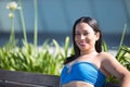 Young, beautiful, brunette, South American woman in a blue dress sitting on a bench looking at the camera smiling and happy Royalty Free Stock Photo