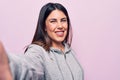 Young beautiful brunette sporty woman make selfie by the camera over pink background looking positive and happy standing and Royalty Free Stock Photo