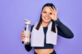 Young beautiful brunette sporty woman using sport towel drinking bottle of water smiling happy doing ok sign with hand on eye Royalty Free Stock Photo