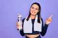 Young beautiful brunette sporty woman using sport towel drinking bottle of water Smiling happy pointing with hand and finger to Royalty Free Stock Photo