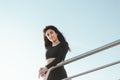 Young beautiful brunette woman in a black sport jumpsuit stands near metal heanrails relaxing after yoga excercising looking at Royalty Free Stock Photo