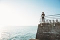 Young beautiful brunette woman in a black sport jumpsuit stands of a stone pier relaxing after yoga excercising looking at the sea