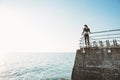 Young beautiful brunette woman in a black sport jumpsuit stands of a stone pier relaxing after yoga excercising looking at the sea Royalty Free Stock Photo