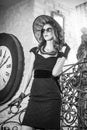 Young beautiful brunette woman in black standing on stairs near an over sized wall clock. Elegant romantic mysterious lady Royalty Free Stock Photo