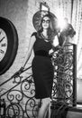 Young beautiful brunette woman in black standing on stairs near an over sized wall clock. Elegant romantic mysterious lady Royalty Free Stock Photo