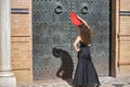 Young, beautiful, brunette woman with black top and skirt, dancing flamenco with a red fan in front of an old, black metal door. Royalty Free Stock Photo