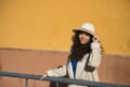 Young, beautiful, brunette woman with curly hair and beige coat and hat, leaning on a railing looking at camera smiling and happy Royalty Free Stock Photo