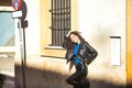 Young, beautiful, brunette woman with curly hair and black leather jacket and pants, leaning against a wall receiving the sun rays Royalty Free Stock Photo