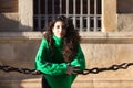 young beautiful brunette woman with curly hair and green woollen coat is leaning on the chains surrounding the cathedral of