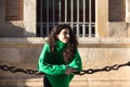 young beautiful brunette woman with curly hair and green woollen coat is leaning on the chains surrounding the cathedral of Royalty Free Stock Photo