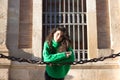 young beautiful brunette woman with curly hair and green woollen coat is leaning on the chains surrounding the cathedral of Royalty Free Stock Photo