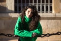 young beautiful brunette woman with curly hair and green woollen coat is leaning on the chains surrounding the cathedral of Royalty Free Stock Photo