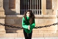 young beautiful brunette woman with curly hair and green woollen coat is leaning on the chains surrounding the cathedral of Royalty Free Stock Photo