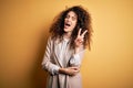 Young beautiful brunette woman with curly hair and piercing wearing casual t-shirt and diadem smiling with happy face winking at Royalty Free Stock Photo