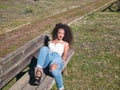 Young, beautiful, brunette woman with curly hair, white top and jeans, lying on a wooden bench with a lost and distracted look. Royalty Free Stock Photo