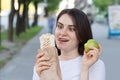 Young beautiful brunette woman on a diet chooses food - what to eat an apple or fast food. Bites the shawarma and