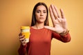 Young beautiful brunette woman drinking cup of takeaway coffe over yellow background with open hand doing stop sign with serious Royalty Free Stock Photo