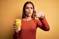 Young beautiful brunette woman drinking cup of takeaway coffe over yellow background pointing with finger to the camera and to Royalty Free Stock Photo