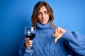 Young beautiful brunette woman drinking glass of red wine over isolated blue background with angry face, negative sign showing Royalty Free Stock Photo