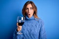 Young beautiful brunette woman drinking glass of red wine over isolated blue background scared in shock with a surprise face, Royalty Free Stock Photo