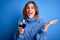 Young beautiful brunette woman drinking glass of red wine over isolated blue background very happy and excited, winner expression Royalty Free Stock Photo