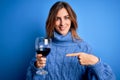 Young beautiful brunette woman drinking glass of red wine over isolated blue background very happy pointing with hand and finger Royalty Free Stock Photo