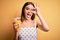 Young beautiful brunette woman drinking healthy orange juice over yellow background with happy face smiling doing ok sign with Royalty Free Stock Photo
