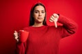 Young beautiful brunette woman drinking mug of coffe over isolated red background with angry face, negative sign showing dislike Royalty Free Stock Photo