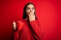 Young beautiful brunette woman drinking mug of coffe over isolated red background cover mouth with hand shocked with shame for Royalty Free Stock Photo