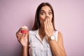 Young beautiful brunette woman eating chocolate cupcake over isolated pink background cover mouth with hand shocked with shame for Royalty Free Stock Photo