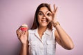 Young beautiful brunette woman eating chocolate cupcake over isolated pink background with happy face smiling doing ok sign with Royalty Free Stock Photo