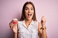 Young beautiful brunette woman eating chocolate cupcake over isolated pink background screaming proud and celebrating victory and Royalty Free Stock Photo