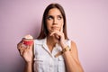 Young beautiful brunette woman eating chocolate cupcake over isolated pink background serious face thinking about question, very Royalty Free Stock Photo