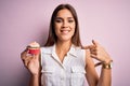 Young beautiful brunette woman eating chocolate cupcake over isolated pink background with surprise face pointing finger to Royalty Free Stock Photo