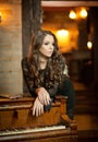 Young beautiful brunette woman in elegant black dress standing near a vintage piano. Sensual romantic lady with long dark hair Royalty Free Stock Photo