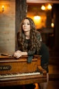 Young beautiful brunette woman in elegant black dress standing near a vintage piano. Sensual romantic lady with long dark hair Royalty Free Stock Photo