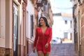 Young, beautiful brunette woman in an elegant red dress, walking at dawn down a lonely street in a beautiful white Andalusian Royalty Free Stock Photo