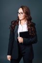 A young beautiful brunette woman in glasses and a business suit smiles and looks away. Studio portrait. Business Coach