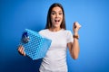 Young beautiful brunette woman holding birthday gift over isolated blue background screaming proud and celebrating victory and Royalty Free Stock Photo