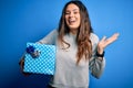 Young beautiful brunette woman holding birthday gift over isolated blue background very happy and excited, winner expression Royalty Free Stock Photo