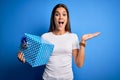 Young beautiful brunette woman holding birthday gift over isolated blue background very happy and excited, winner expression Royalty Free Stock Photo