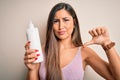 Young beautiful brunette woman holding bottle of body cream over isolated white background with angry face, negative sign showing