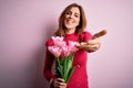 Young beautiful brunette woman holding bouquet of pink tulips over isolated background smiling cheerful offering palm hand giving Royalty Free Stock Photo